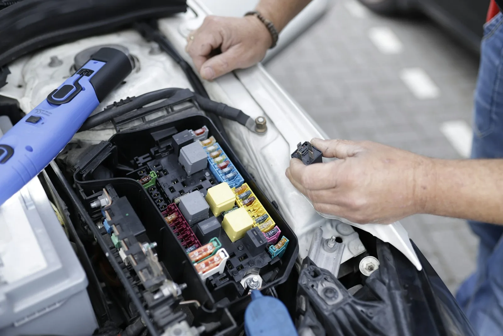 A mechanic's hands inspecting a car's fuse box