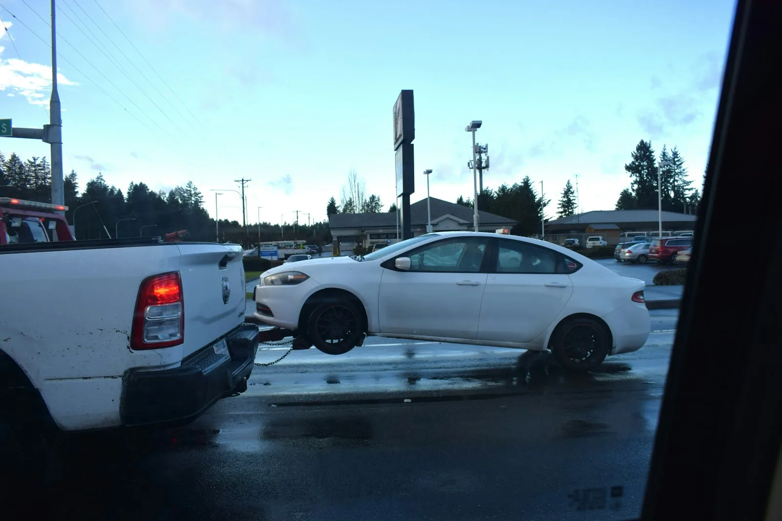 A car being towed on a flatbed pickup truck on a wet road